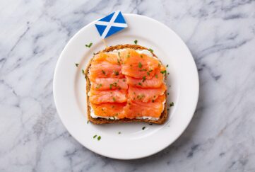 Sandwich, toast with smoked salmon and cream cheese on white plate, with Scottish flag. Marble background. Top view.